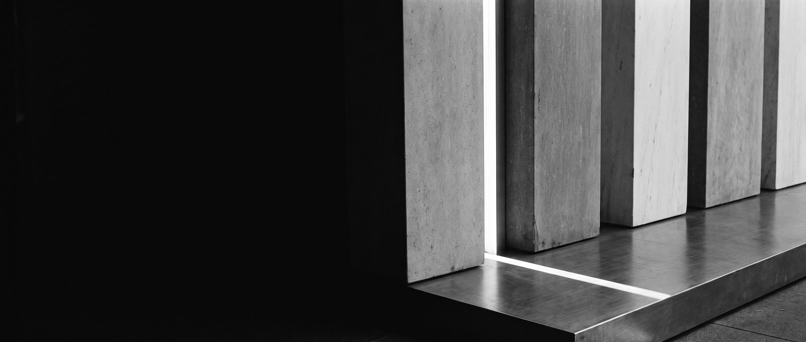 Conceptual editorial illustration — heavy sculptural planes with a narrow opening where a single shaft of daylight cuts through. Monochrome architectural study of capital finding a new path; not a photograph of a real facility.